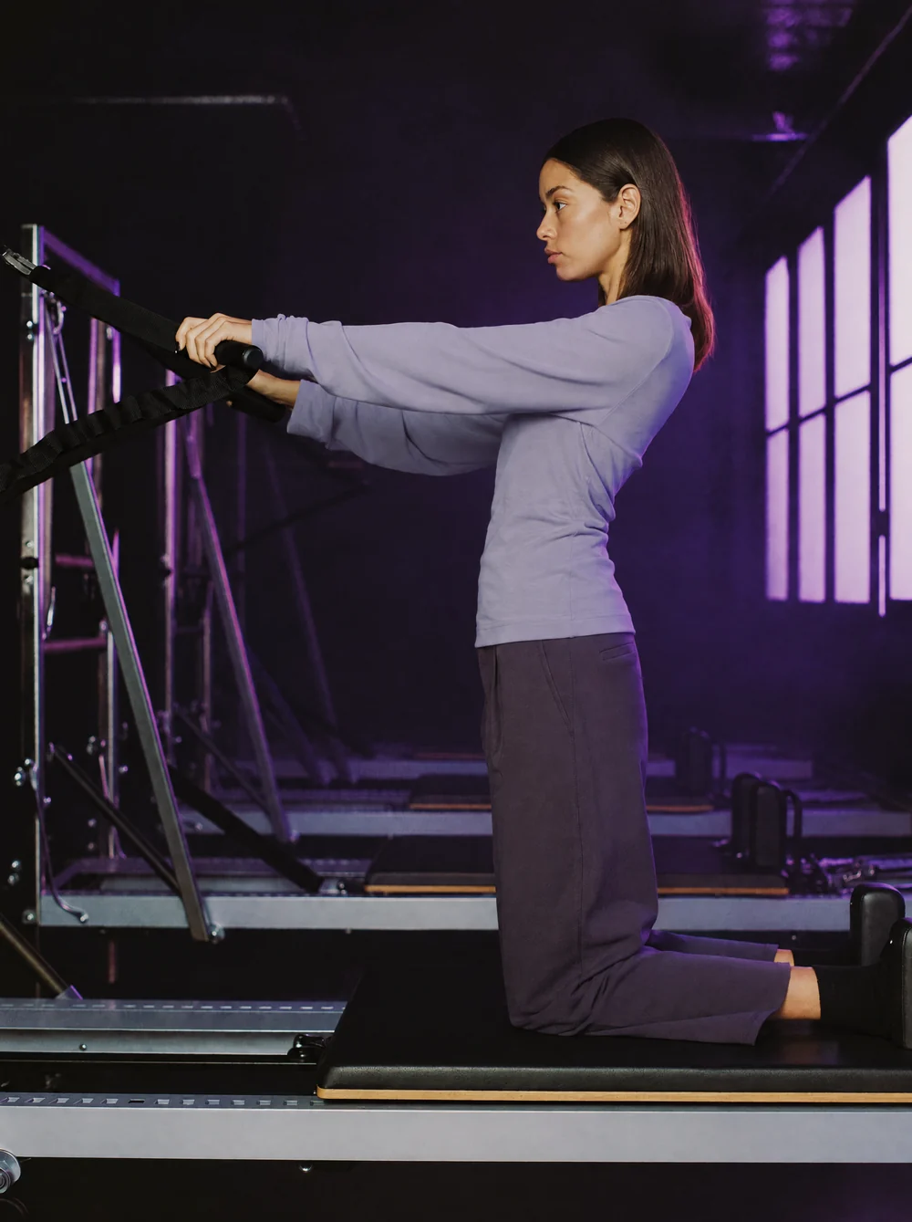 Mulher puxando as alças do reformer em estúdio de pilates com luz lilás