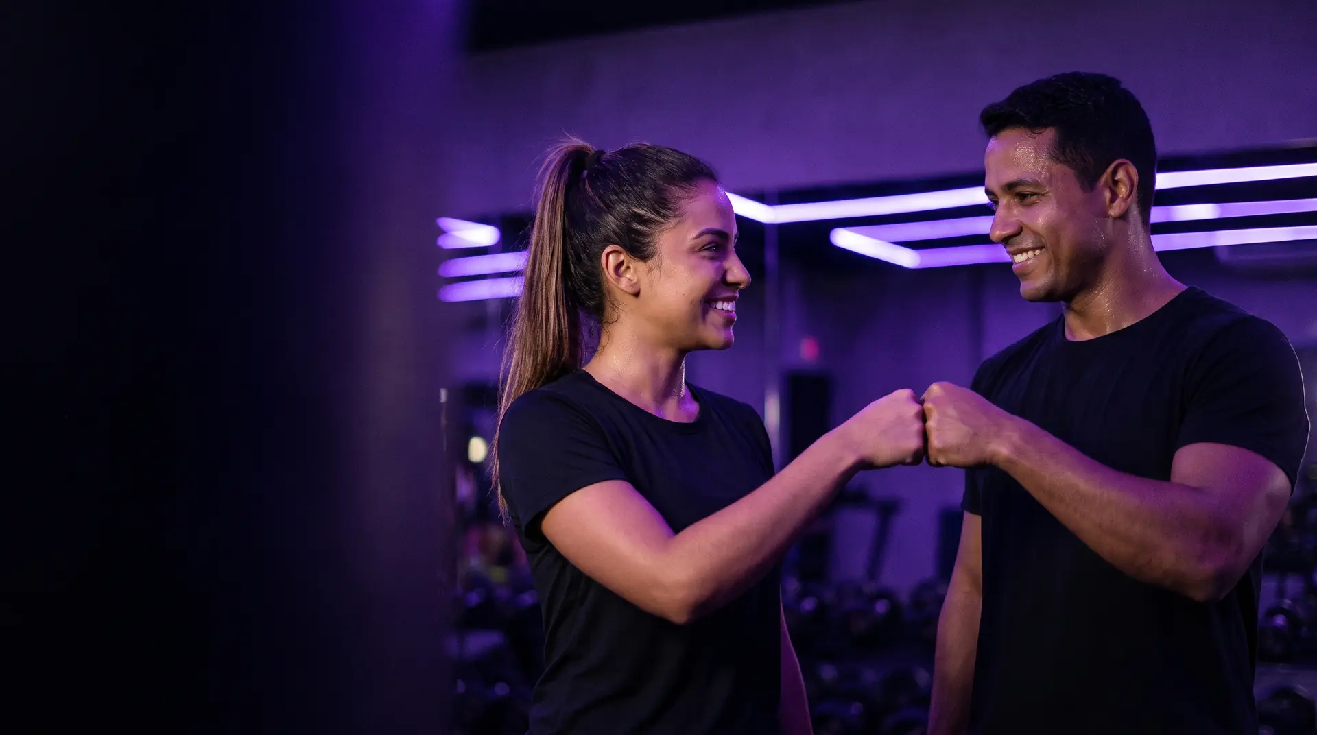 Dois colegas sorrindo e batendo os punhos em uma academia.