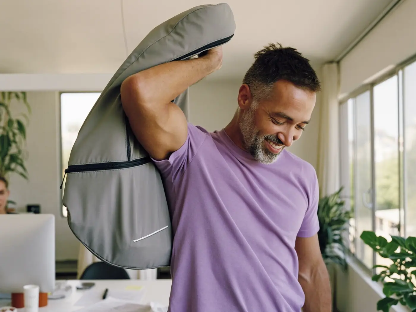 Homem sorrindo em um escritório claro, com uma bolsa de academia no ombro.