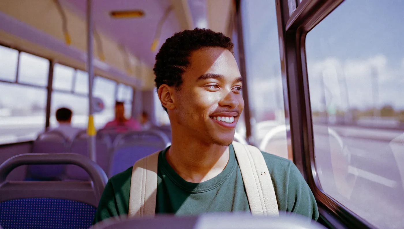 Jovem vai para o trabalho de ônibus, sentado à janela